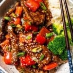Overhead view of Beijing beef served over rice with a side of steamed broccoli in a bowl, with a set of chopsticks on the side.