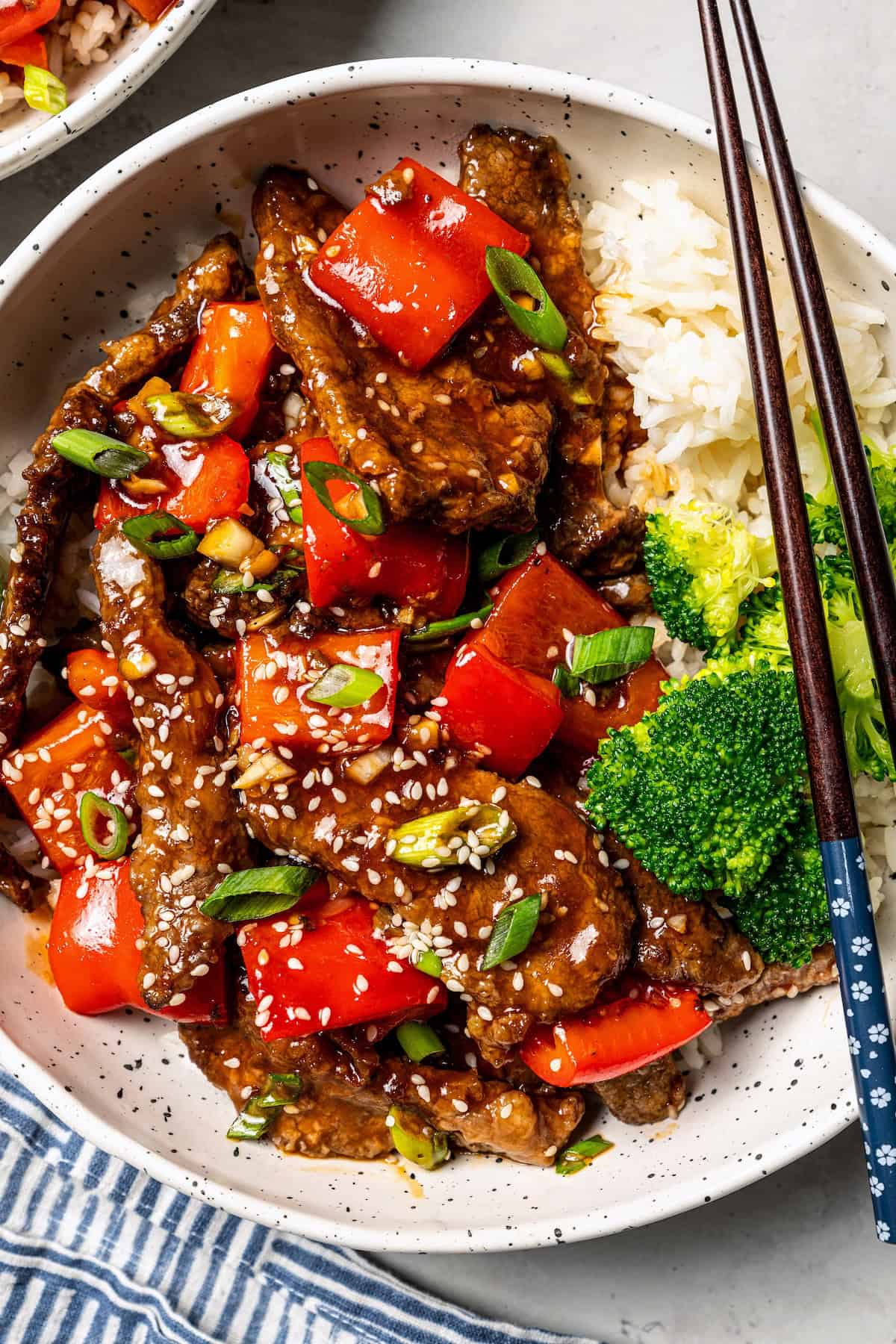 Overhead view of Beijing beef served over rice with a side of steamed broccoli in a bowl, with a set of chopsticks on the side.