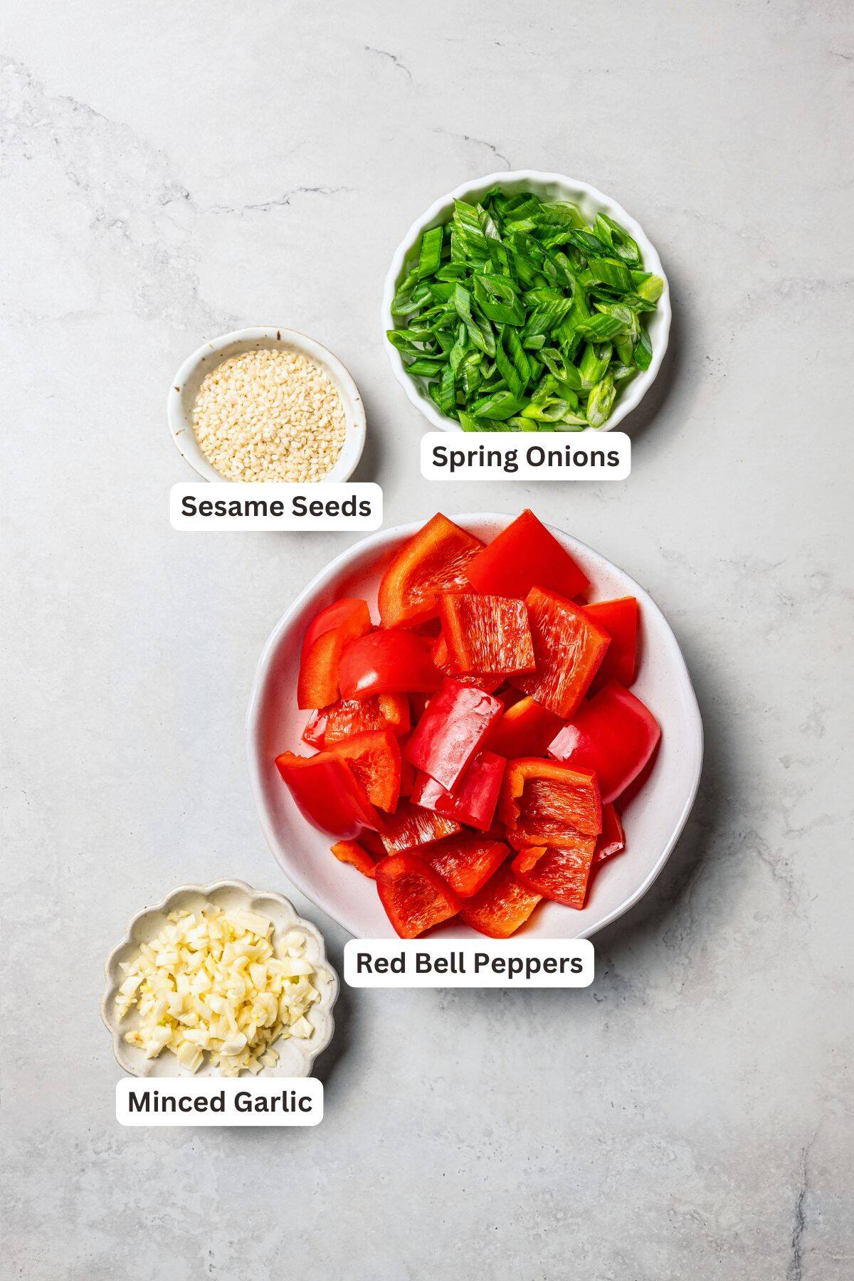 Bell peppers, green onions, sesame seeds, and garlic in bowls with text labels overlaying each ingredient.