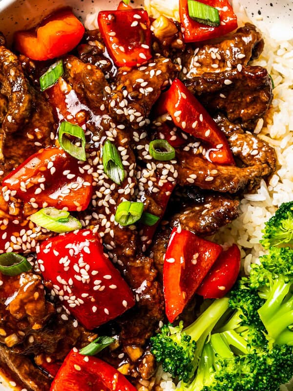Overhead view of Beijing beef served over rice with a side of steamed broccoli in a bowl.