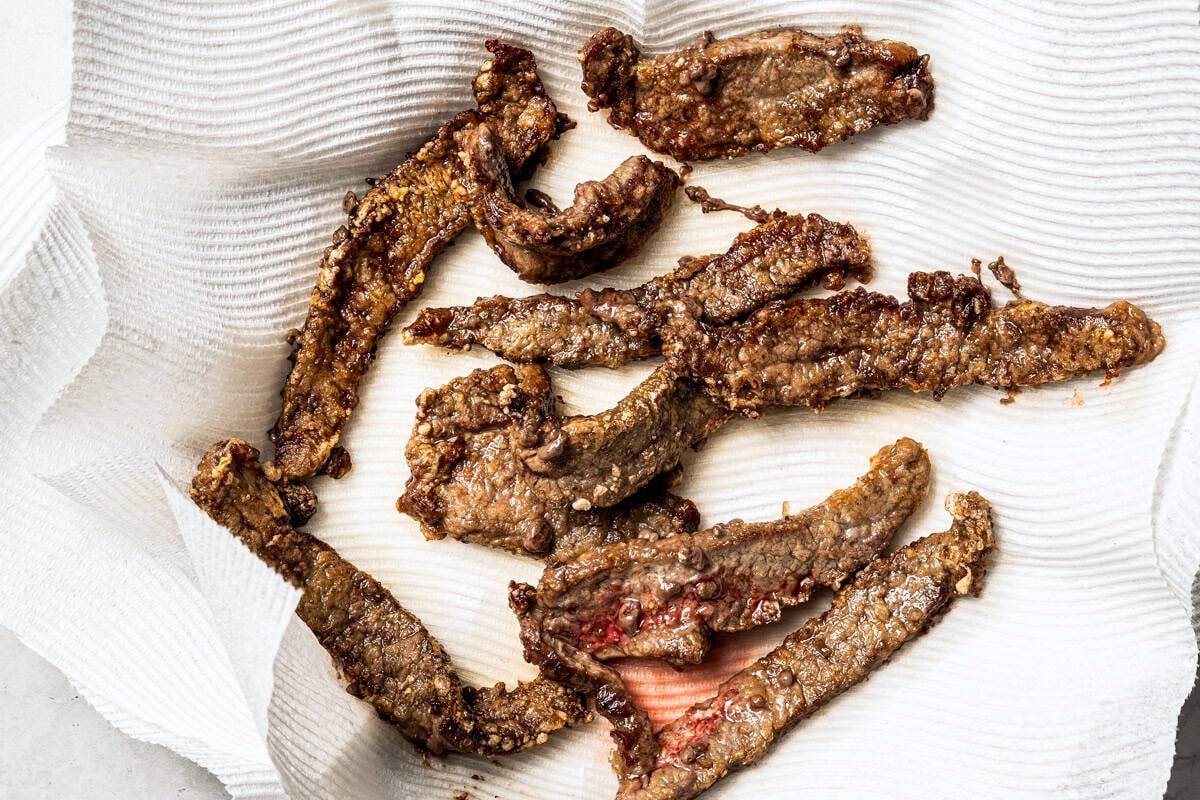 Pan-fried beef strips draining on top of paper towels.