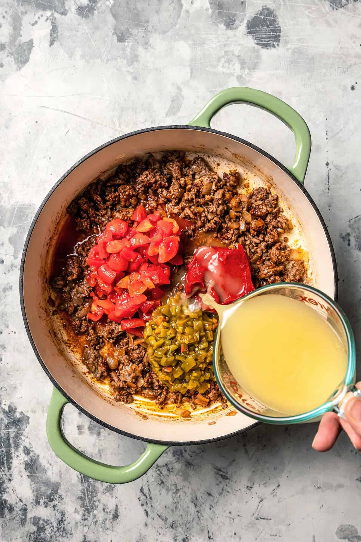 Vegetable broth added to a pot with browned beef, canned tomatoes, and green chilies.