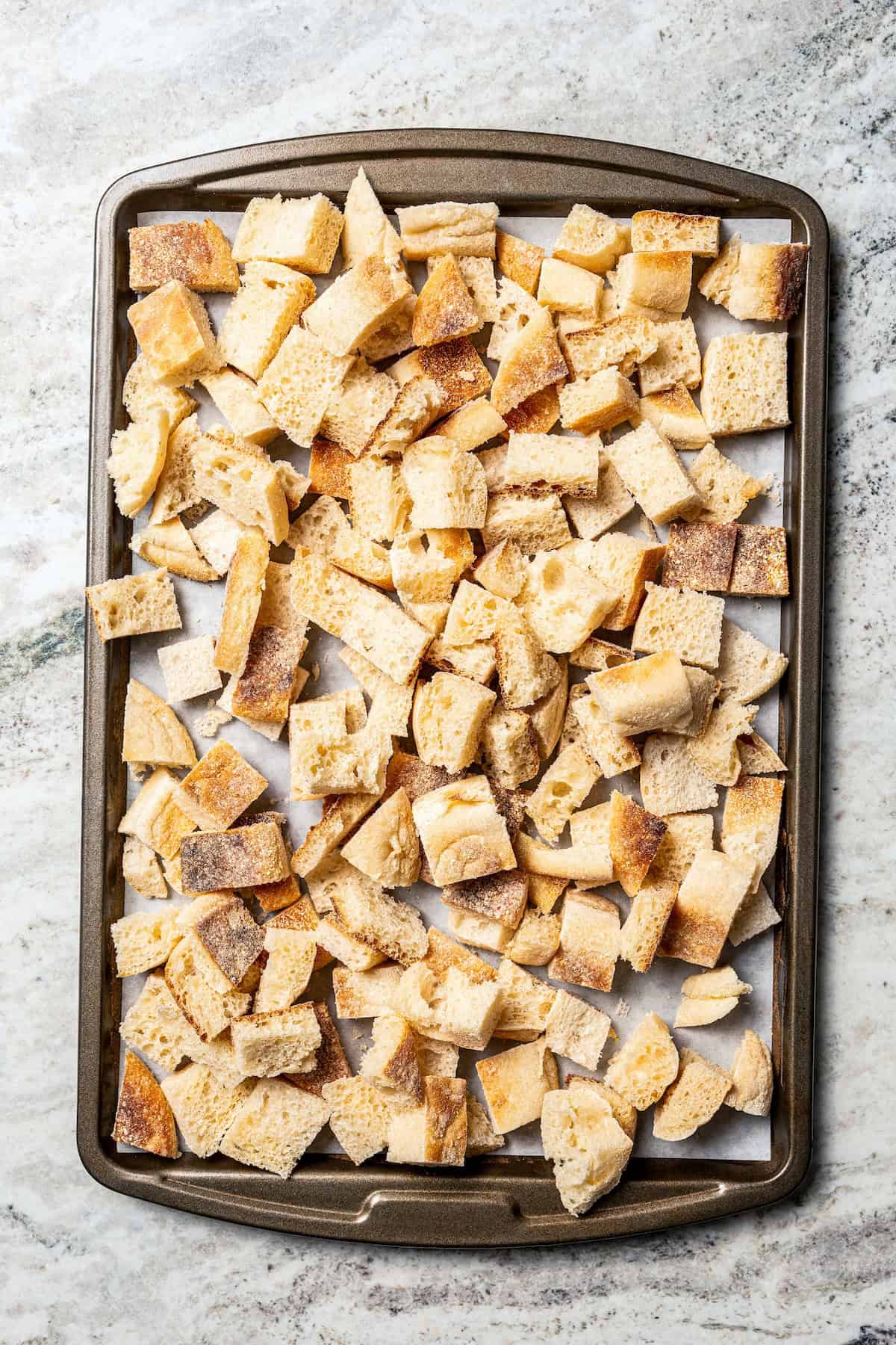 Cubed English muffins spread out on a baking sheet.