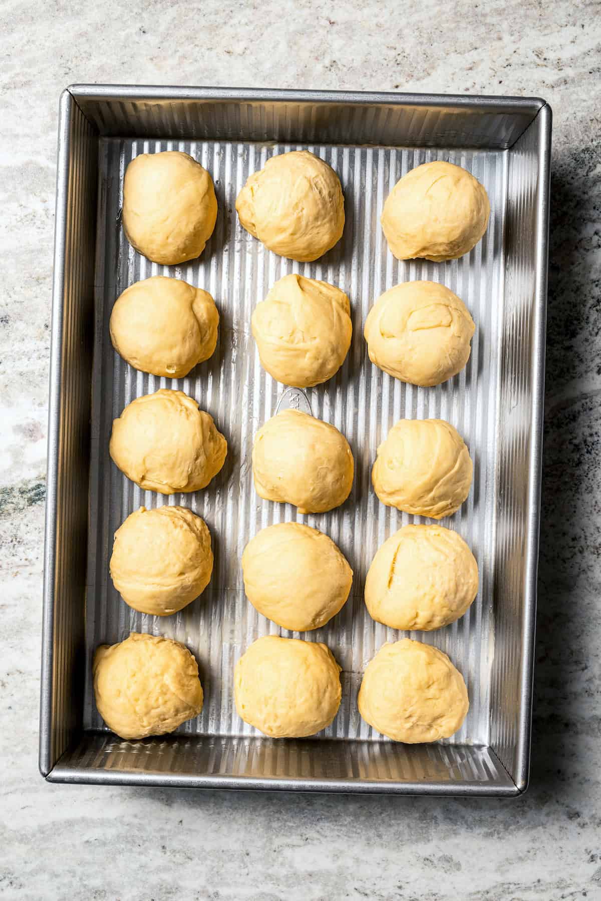 Hawaiian roll dough balls inside a baking tray.