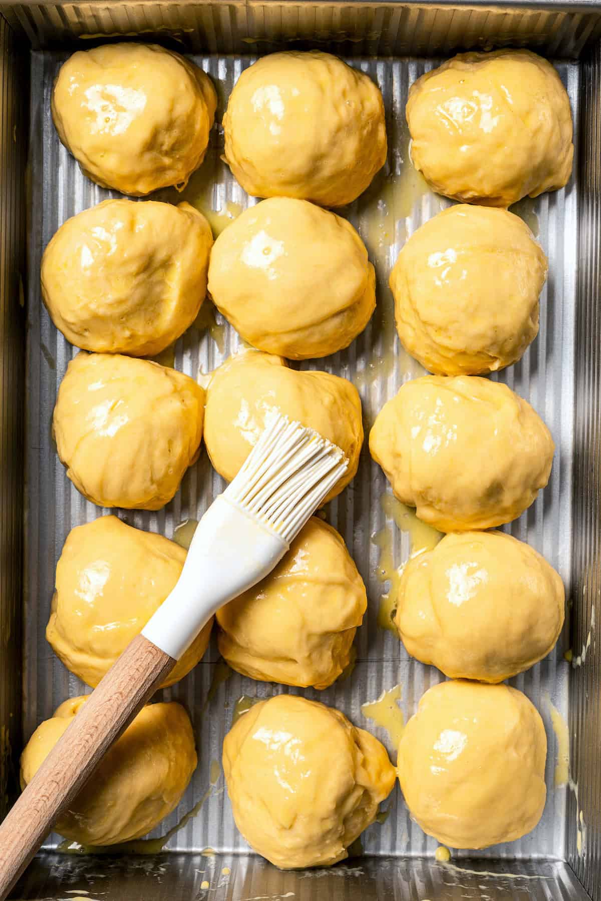 A basting brush coating unbaked Hawaiian rolls with egg wash.