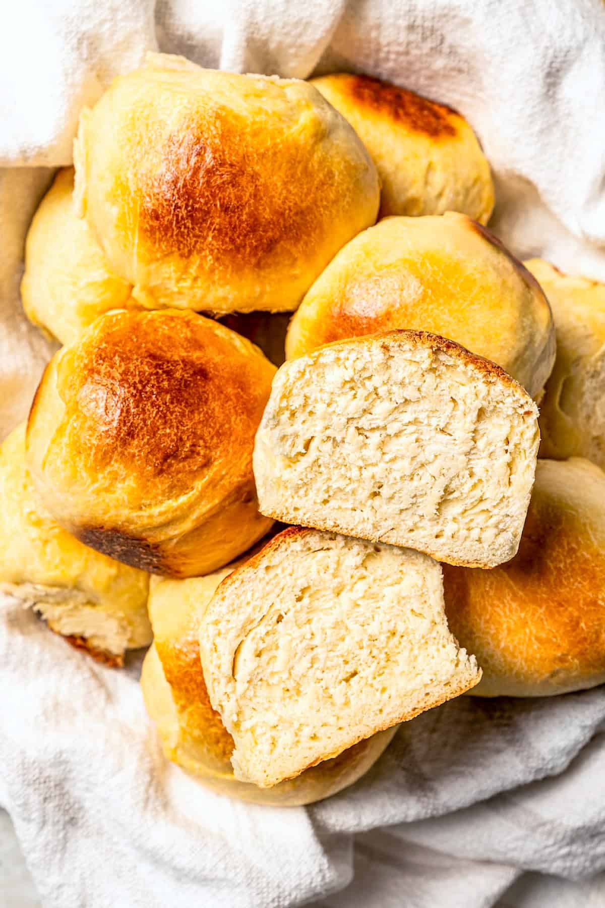 Overhead view of Hawaiian rolls piled in a towel-lined basket, with one roll cut in half to show the fluffy, soft interior.