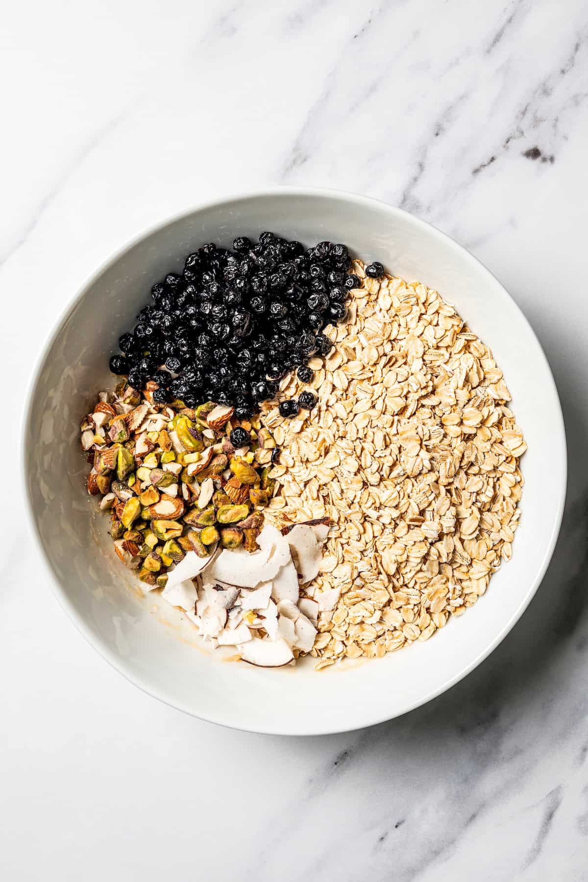 This homemade granola recipe with rolled oats, maple syrup, and brown sugar is sweet, crunchy, and you can make a big batch in the oven! Granola ingredients combined in a bowl.