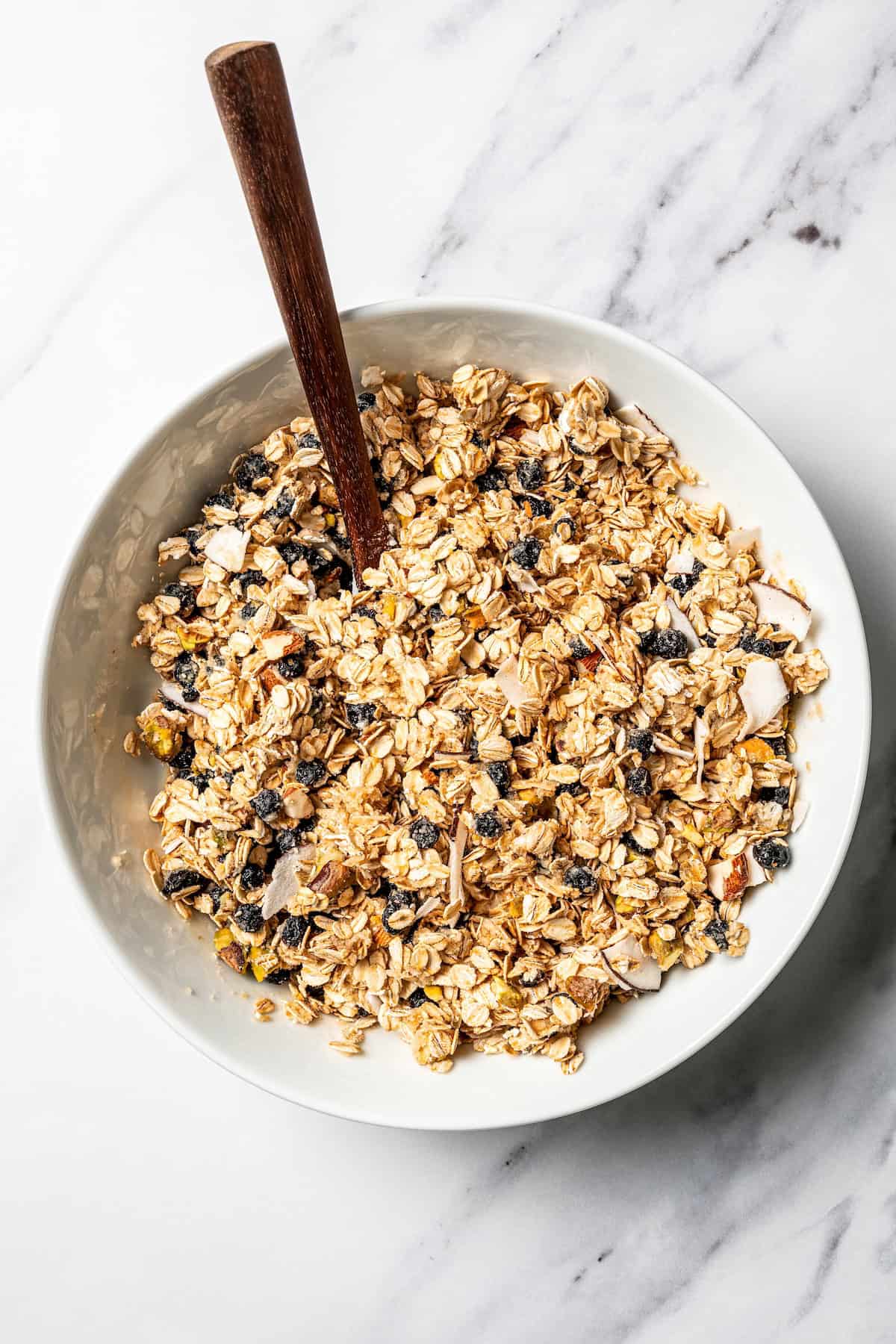 This homemade granola recipe with rolled oats, maple syrup, and brown sugar is sweet, crunchy, and you can make a big batch in the oven! Homemade granola mixture in a bowl with a spoon.