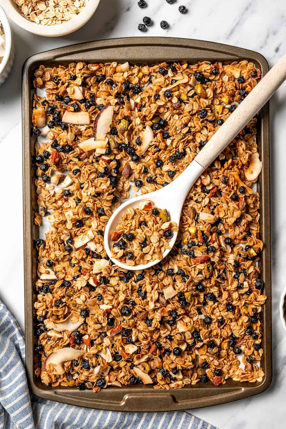 This homemade granola recipe with rolled oats, maple syrup, and brown sugar is sweet, crunchy, and you can make a big batch in the oven! Overhead view of a spoon resting in a baking sheet of baked homemade granola.