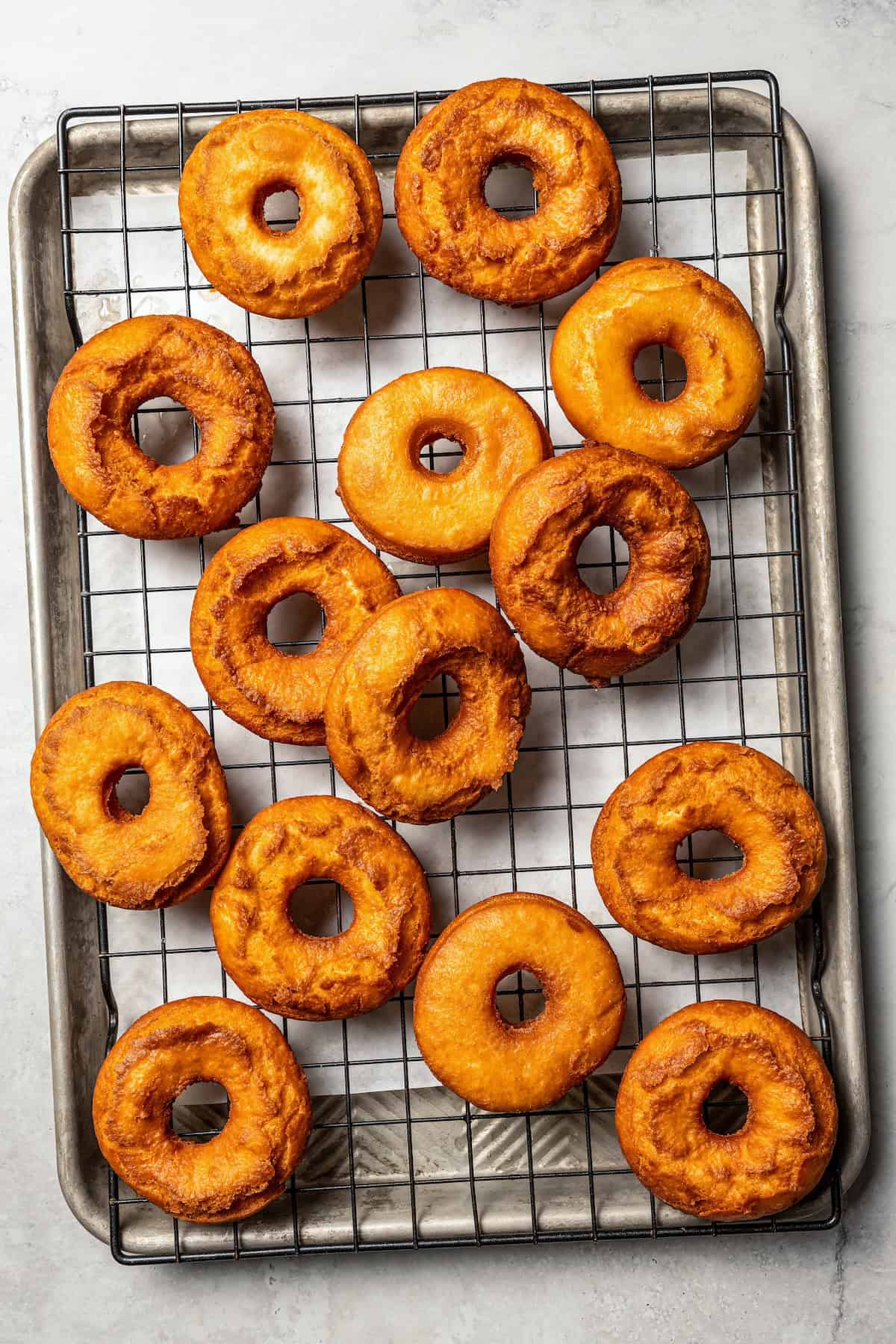 These old-fashioned sour cream donuts are soft and cakey beneath a golden crust coated in creamy vanilla glaze. No yeast or rising time! Fried sour cream donuts on a wire rack.