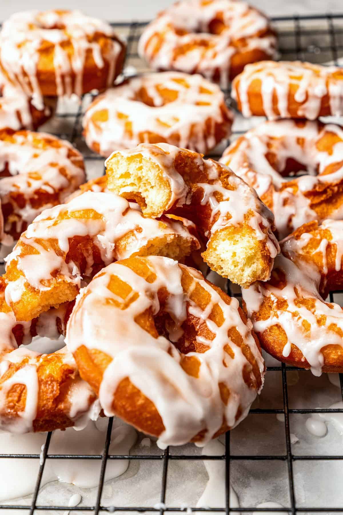These old-fashioned sour cream donuts are soft and cakey beneath a golden crust coated in creamy vanilla glaze. No yeast or rising time! Assorted glazed sour cream donuts on a wire rack.