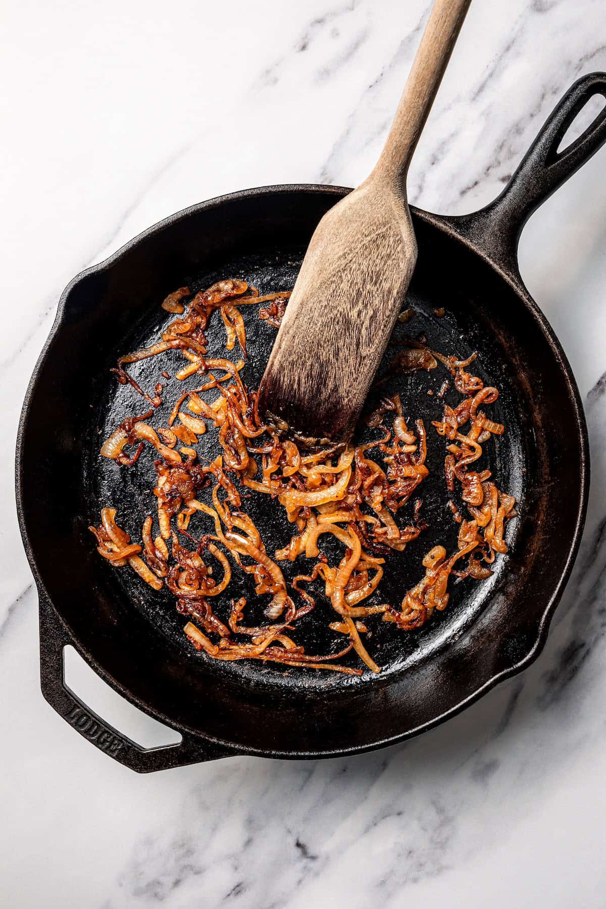 A wooden spatula stirring caramelized onions in a skillet.