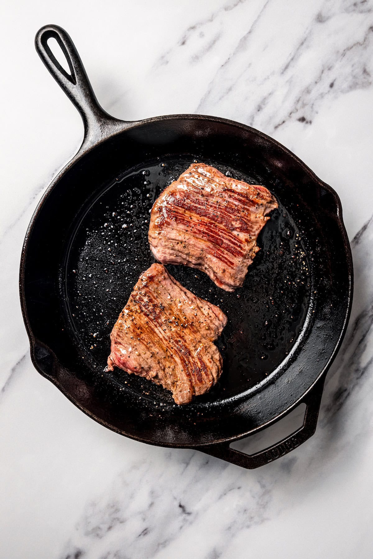 Two seared skirt steaks in a cast iron pan.