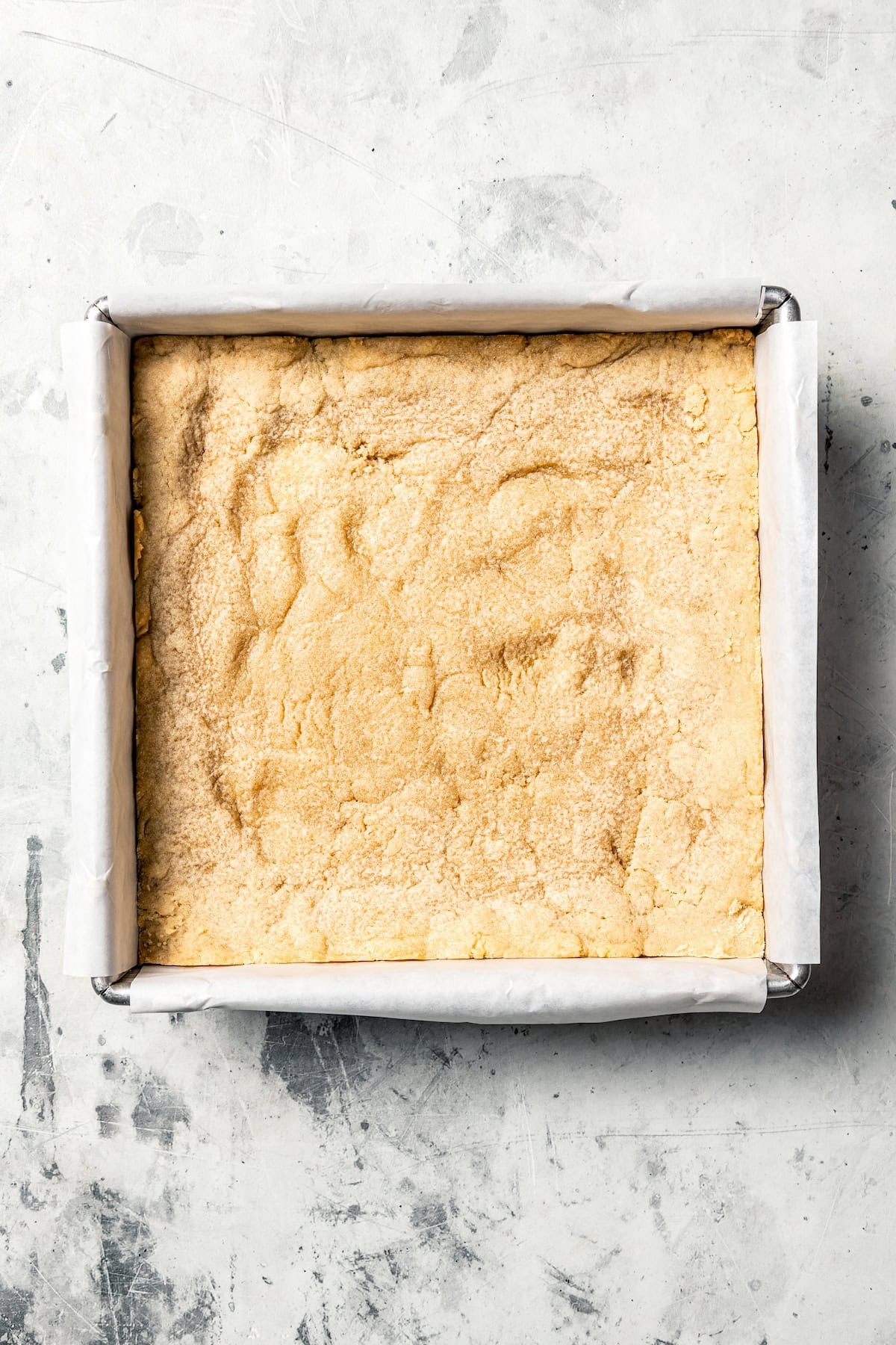 Mixing cookie butter into the dough makes the best sugar cookie bars ever! These bars are soft and chewy, topped with creamy frosting. Sugar cookie dough pressed into a lined square baking pan.