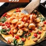 A pan of shrimp in cream sauce with grape tomatoes and baby spinach.