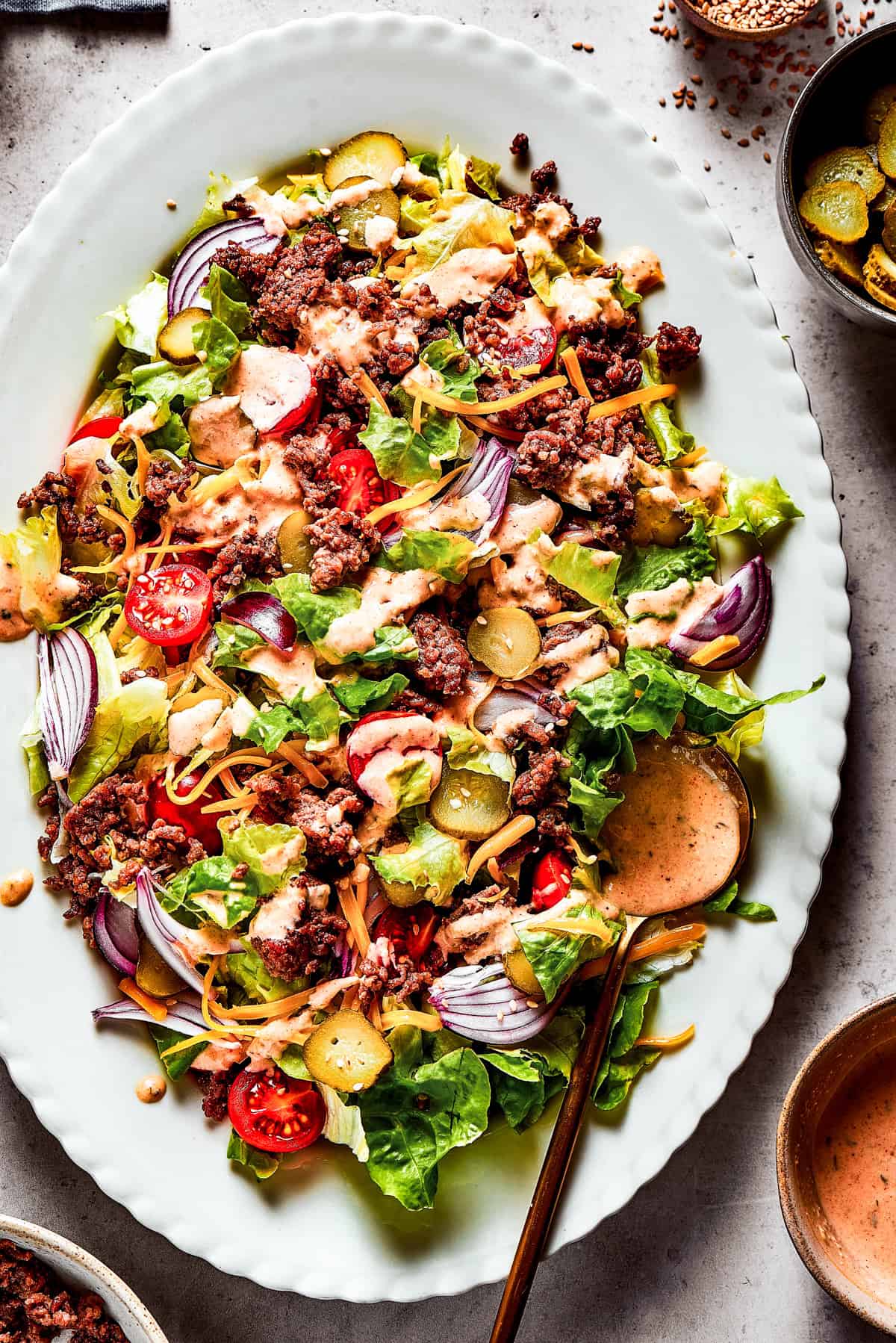 Weekly Menu Plan Salad greens tossed with ground beef, cheese, tomatoes, pickles, and onions served on a platter.