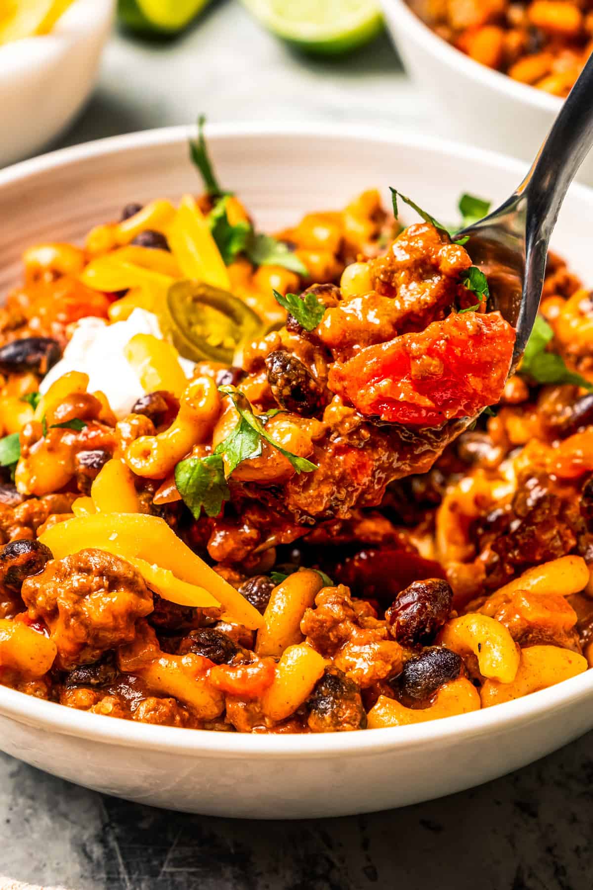 A spoon lifting up chili mac from a bowl.