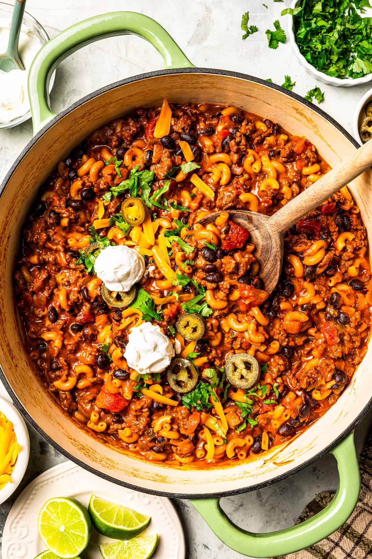 Chili mac in a pot, garnished with sour cream, jalapeños slices, shredded cheese, and cilantro.
