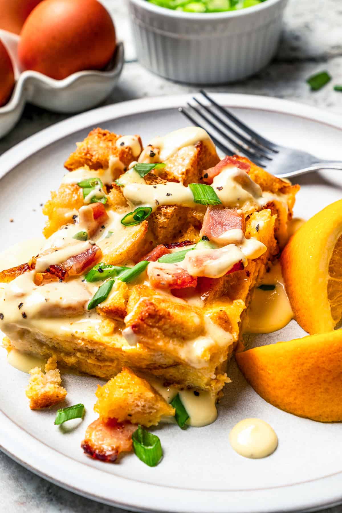 A slice of Eggs Benedict casserole served on a plate with orange slices.