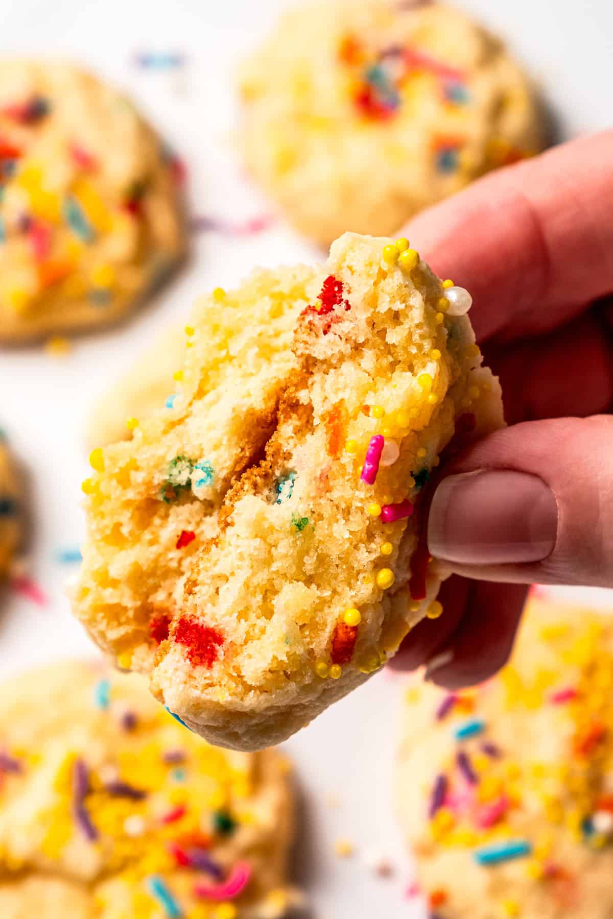 Close-up of a hand holding up a funfetti cookie broken in half to expose the thick center.