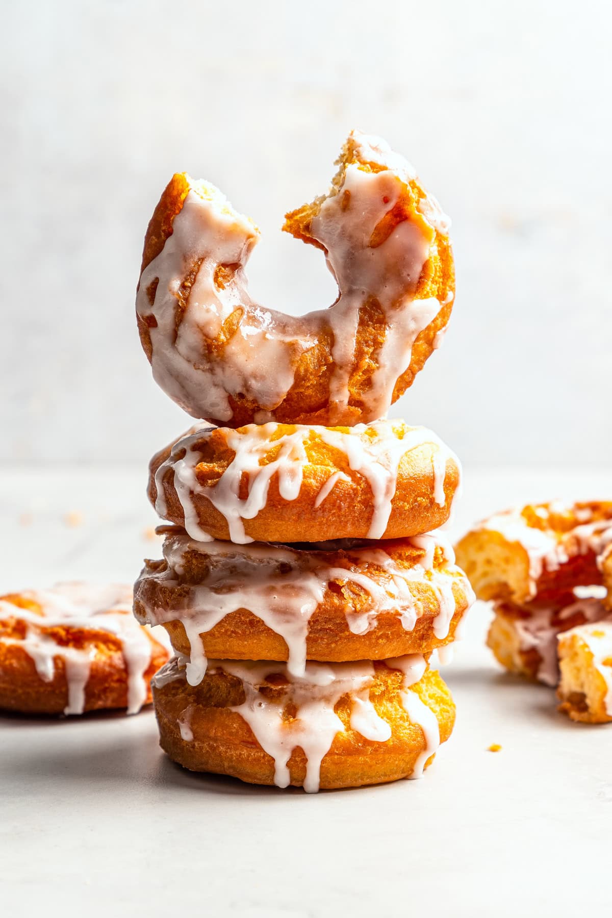 These old-fashioned sour cream donuts are soft and cakey beneath a golden crust coated in creamy vanilla glaze. No yeast or rising time! Three glazed sour cream donuts stacked, with a fourth donut with a bite missing on top.