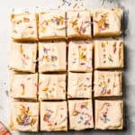 Overhead view of sugar cookie bars topped with frosting and sprinkles, cut into squares.