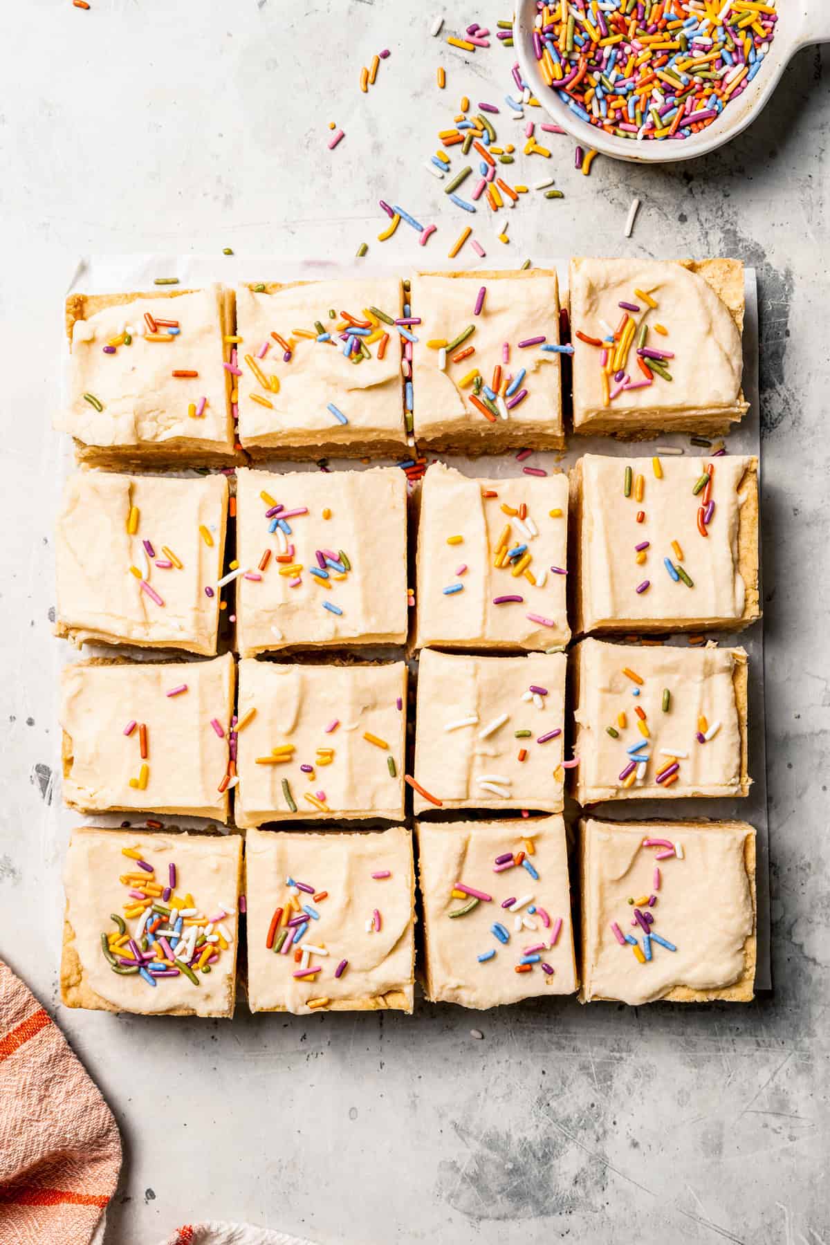 Mixing cookie butter into the dough makes the best sugar cookie bars ever! These bars are soft and chewy, topped with creamy frosting. Overhead view of sugar cookie bars topped with frosting and sprinkles, cut into squares.