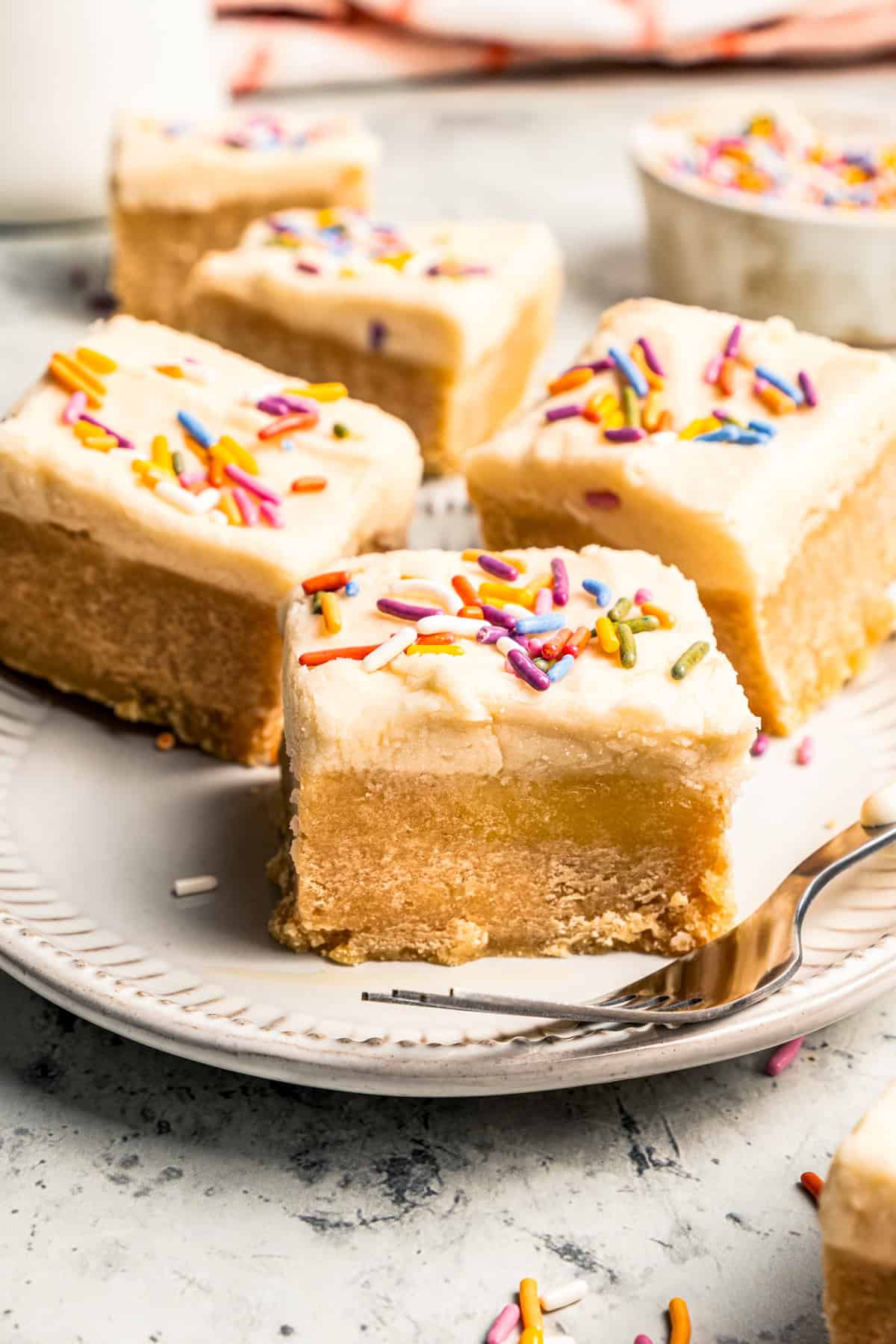 Mixing cookie butter into the dough makes the best sugar cookie bars ever! These bars are soft and chewy, topped with creamy frosting. Four frosted sugar cookie bars served on a plate.
