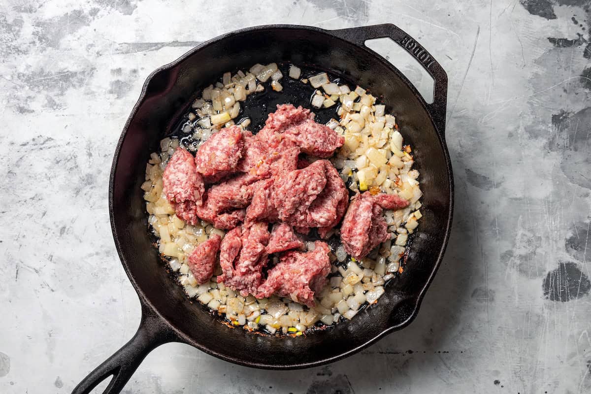 Ground breakfast sausage added to sautéed onions in a skillet.