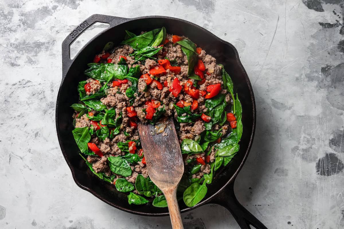Spinach and peppers added to browned breakfast sausage in a skillet.