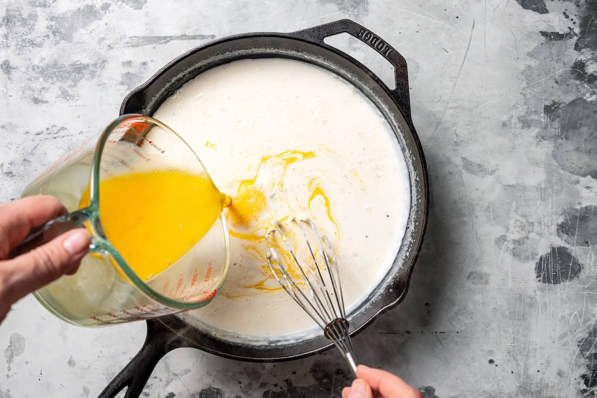 Beaten eggs being poured into the cream sauce in a skillet.