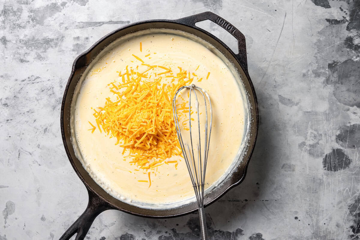 Shredded cheese added to cream sauce in a skillet.