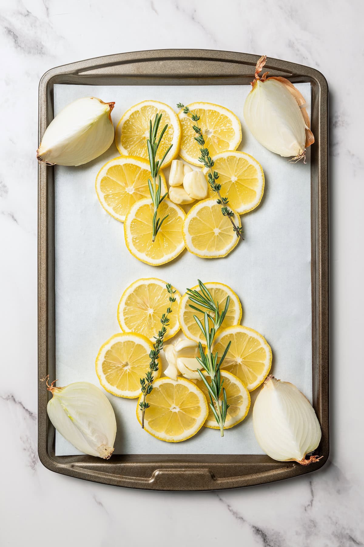 This easy Cornish hen recipe is perfectly juicy and golden-brown, rubbed with savory spices and oven-roasted over a bed of lemon and herbs. Lemon slices, fresh herbs, and quartered onions arranged on a baking sheet.