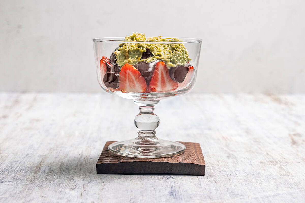 Pistachio filling layered over melted chocolate and chopped strawberries in a dessert glass.