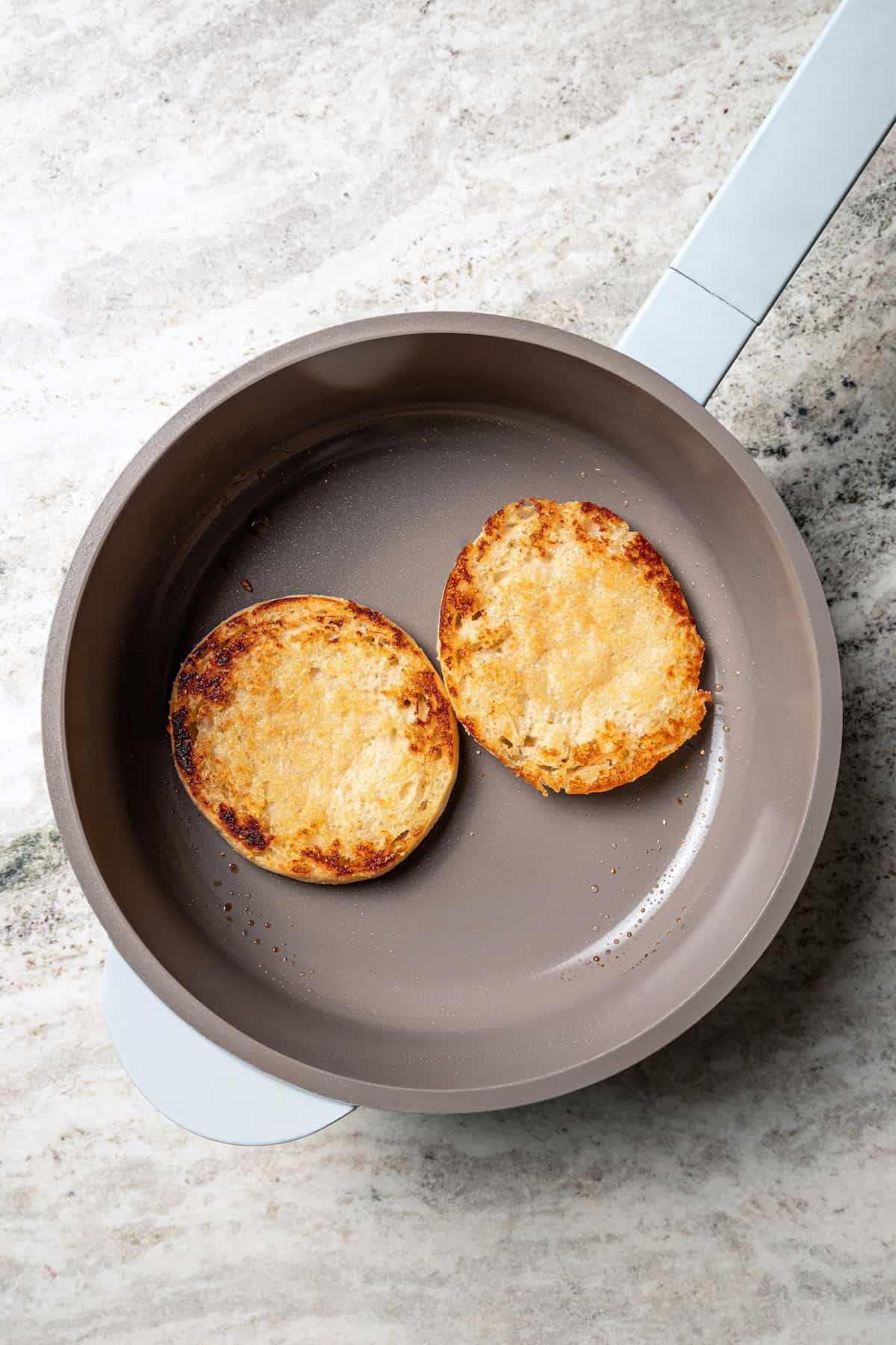 Two toasted English muffin halves in a skillet.