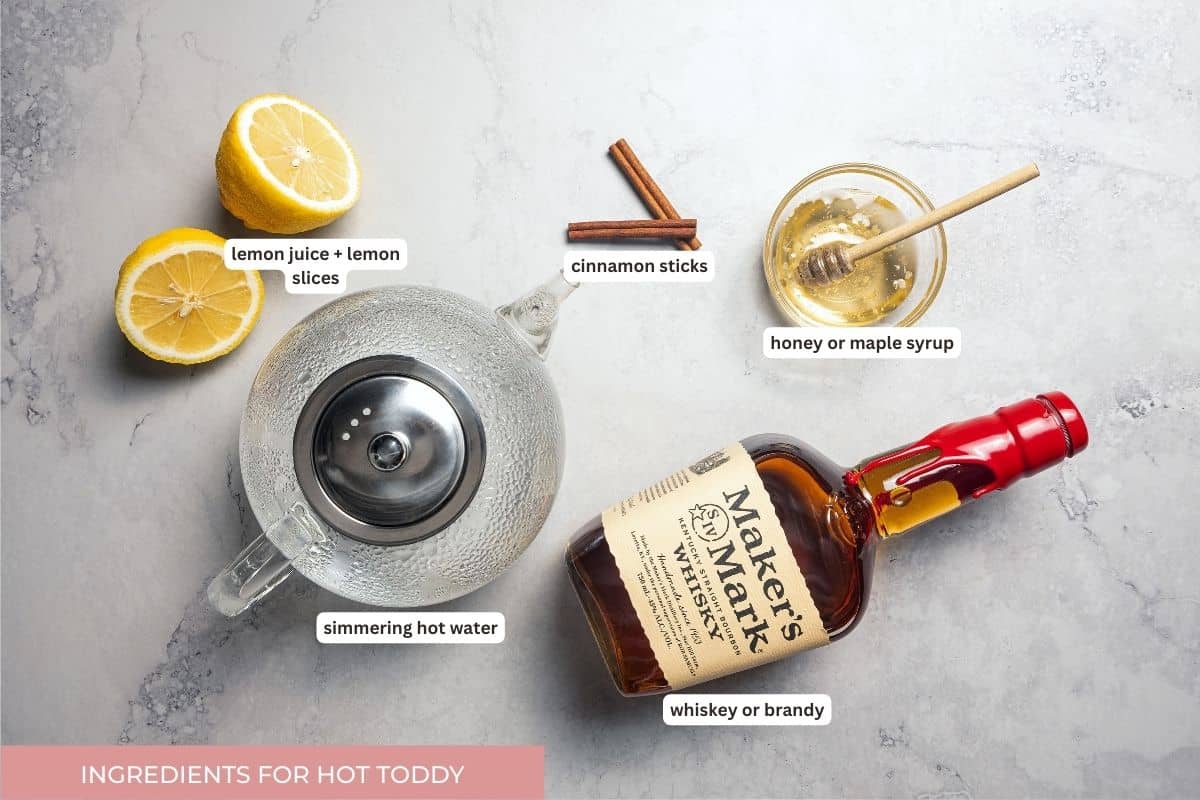 This classic hot toddy recipe is a soothing blend of your favorite whiskey, a drop of honey, and a squeeze of lemon juice with hot water. Hot toddy ingredients with text labels overlaying each ingredient.