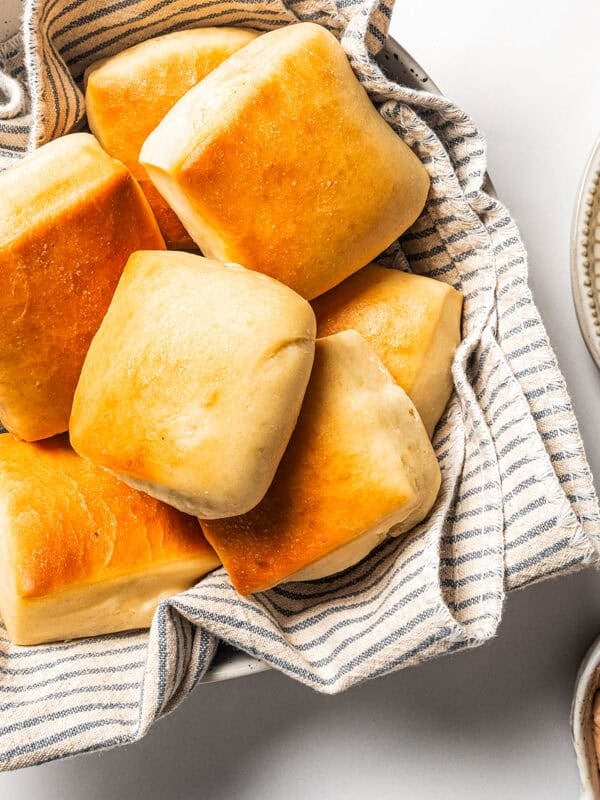 Texas Roadhouse rolls in a bowl lined with a dishcloth next to a sliced roll topped with cinnamon butter on a plate.