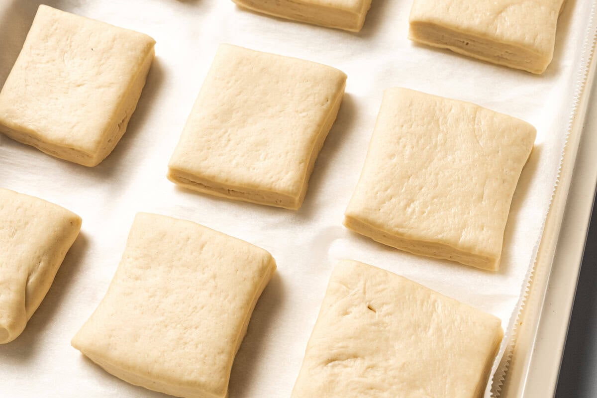 Dough is cut into squares and arranged in rows on a baking sheet to make Texas Roadhouse bread rolls.