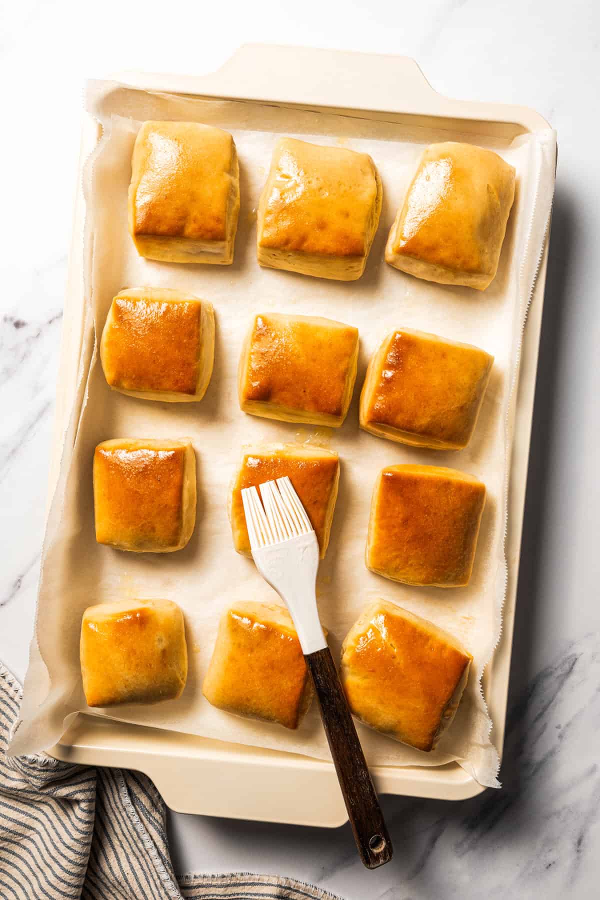 Brushing melted butter over freshly baked Texas Roadhouse rolls.