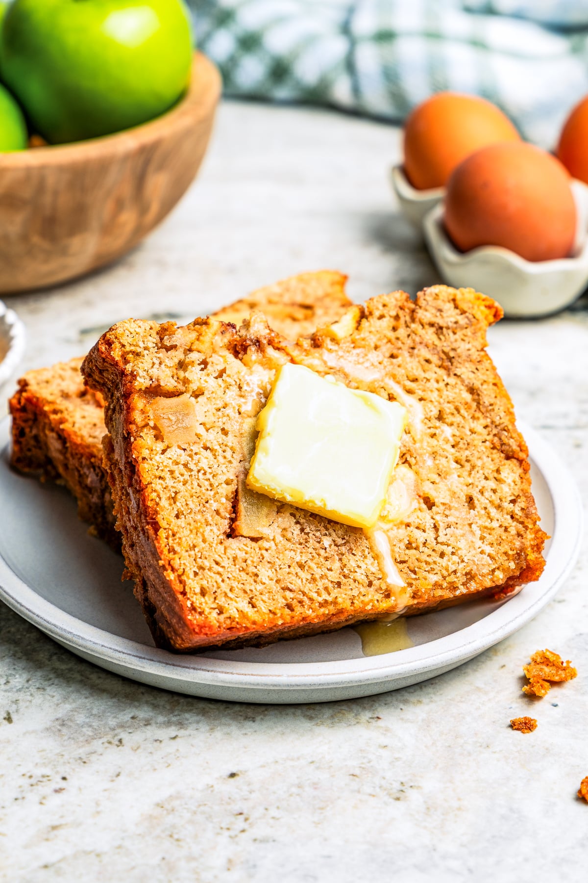 A pat of butter melting on a slice of apple bread, propped up against a second slice on a plate.