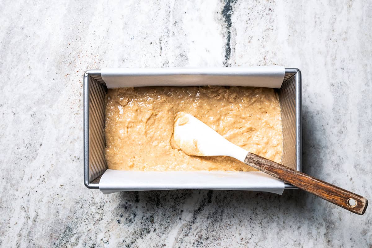 Apple bread batter spread into the bottom of a loaf pan.