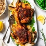 Two Cornish hens on a platter, with a bowl of rice set on one side of the platter, and a bowl of cooked green beans in another bowl.