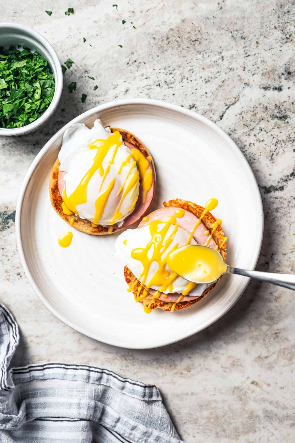 Using a spoon to drizzle Hollandaise sauce over eggs Benedict.