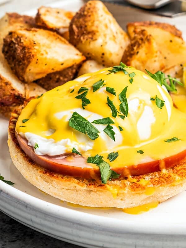 Eggs Benedict topped with Hollandaise sauce and served with crispy breakfast potatoes on a plate.