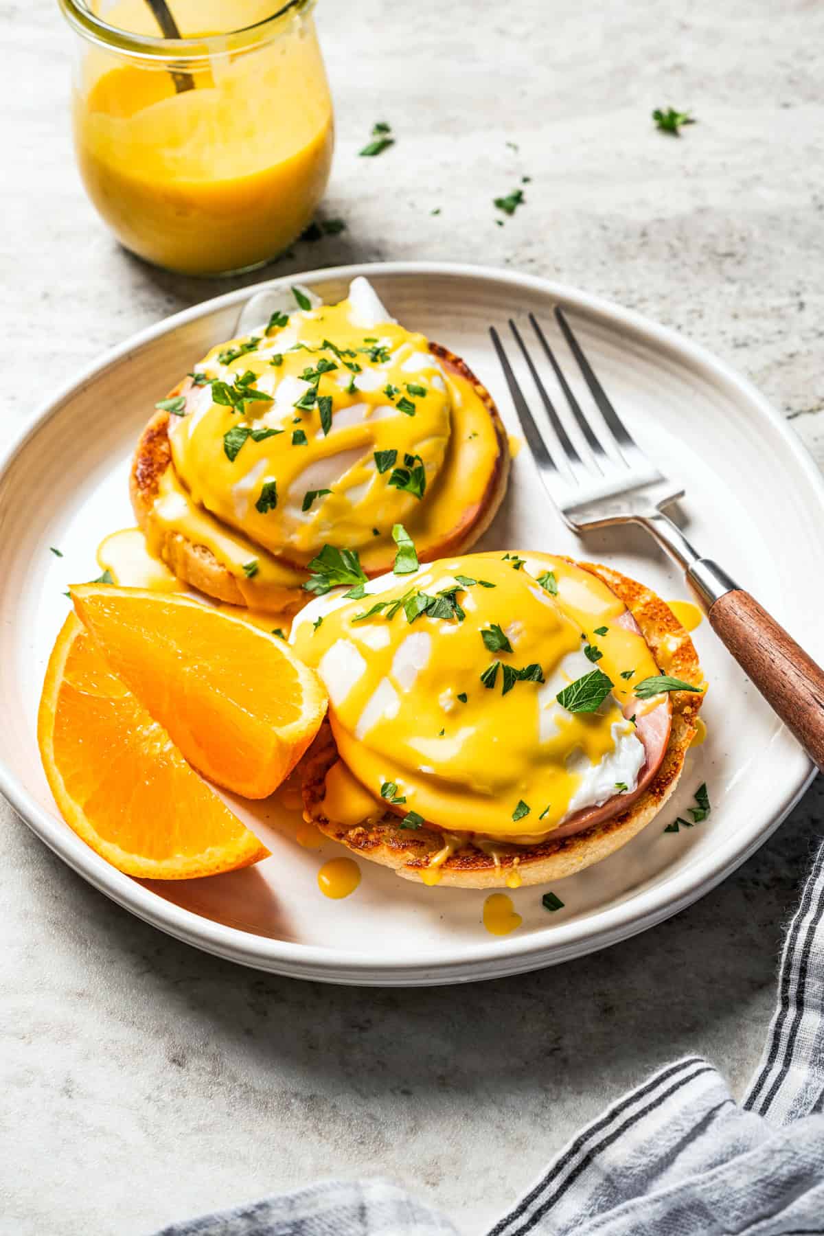 Weekly Meal Plan Eggs Benedict served with orange wedges on a plate next to a jar of Hollandaise sauce.