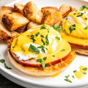 Eggs Benedict topped with Hollandaise sauce and served with crispy breakfast potatoes on a plate.