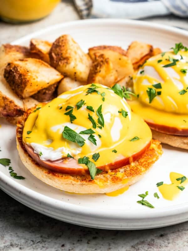 Eggs Benedict topped with Hollandaise sauce and served with crispy breakfast potatoes on a plate.
