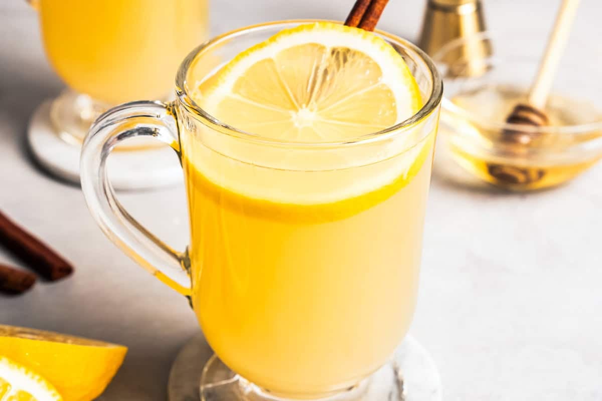 A classic hot toddy in a glass mug garnished with a fresh lemon slice and a cinnamon stick.