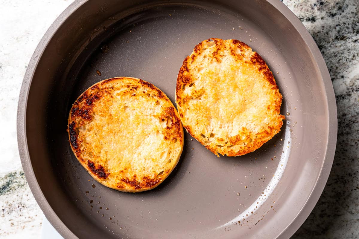 Two toasted English muffin halves in a skillet.