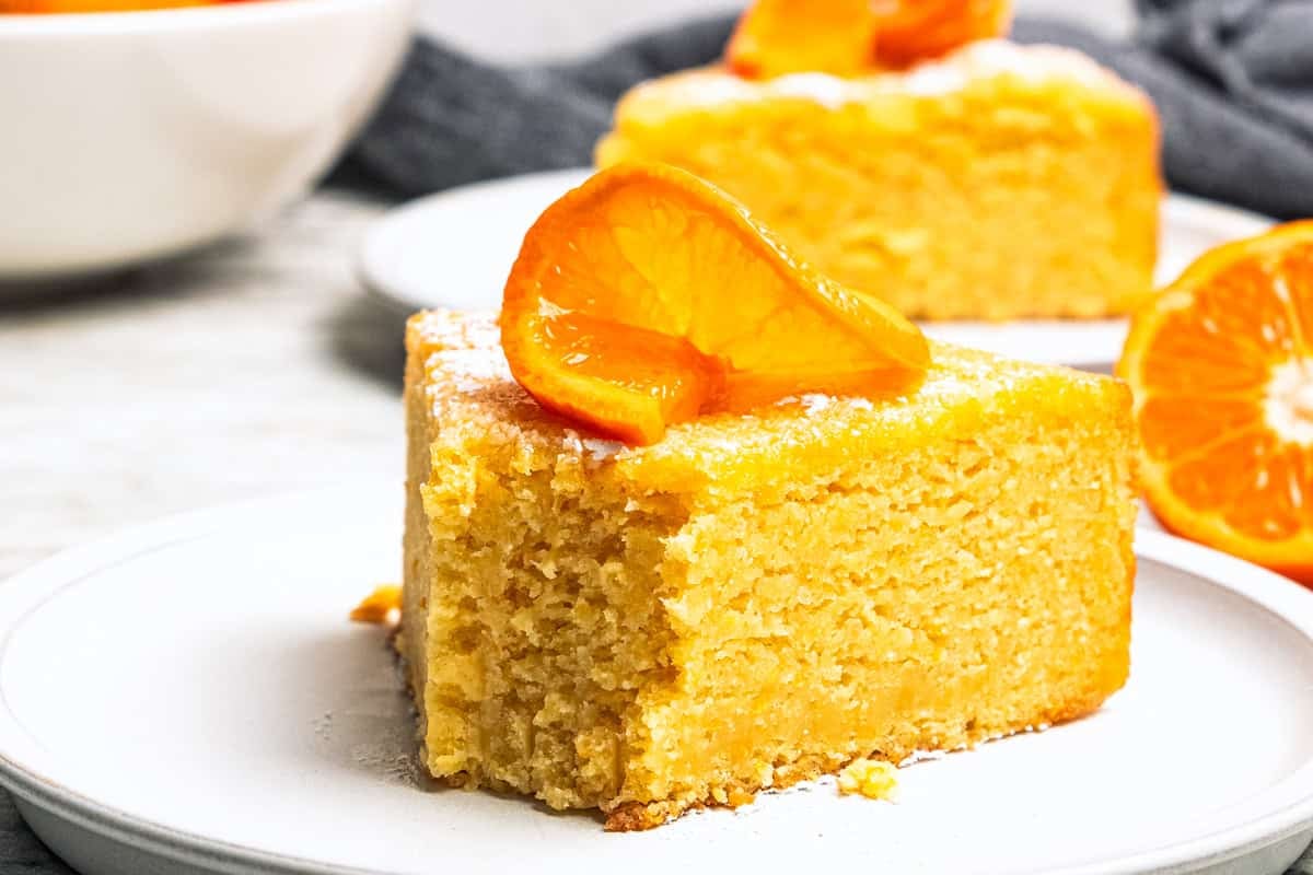 This orange cake recipe uses whole oranges, peels and all! It's moist and full of sweet citrus flavor, drenched in orange glaze. A slice of orange cake with a forkful missing from the end to expose the moist crumb.